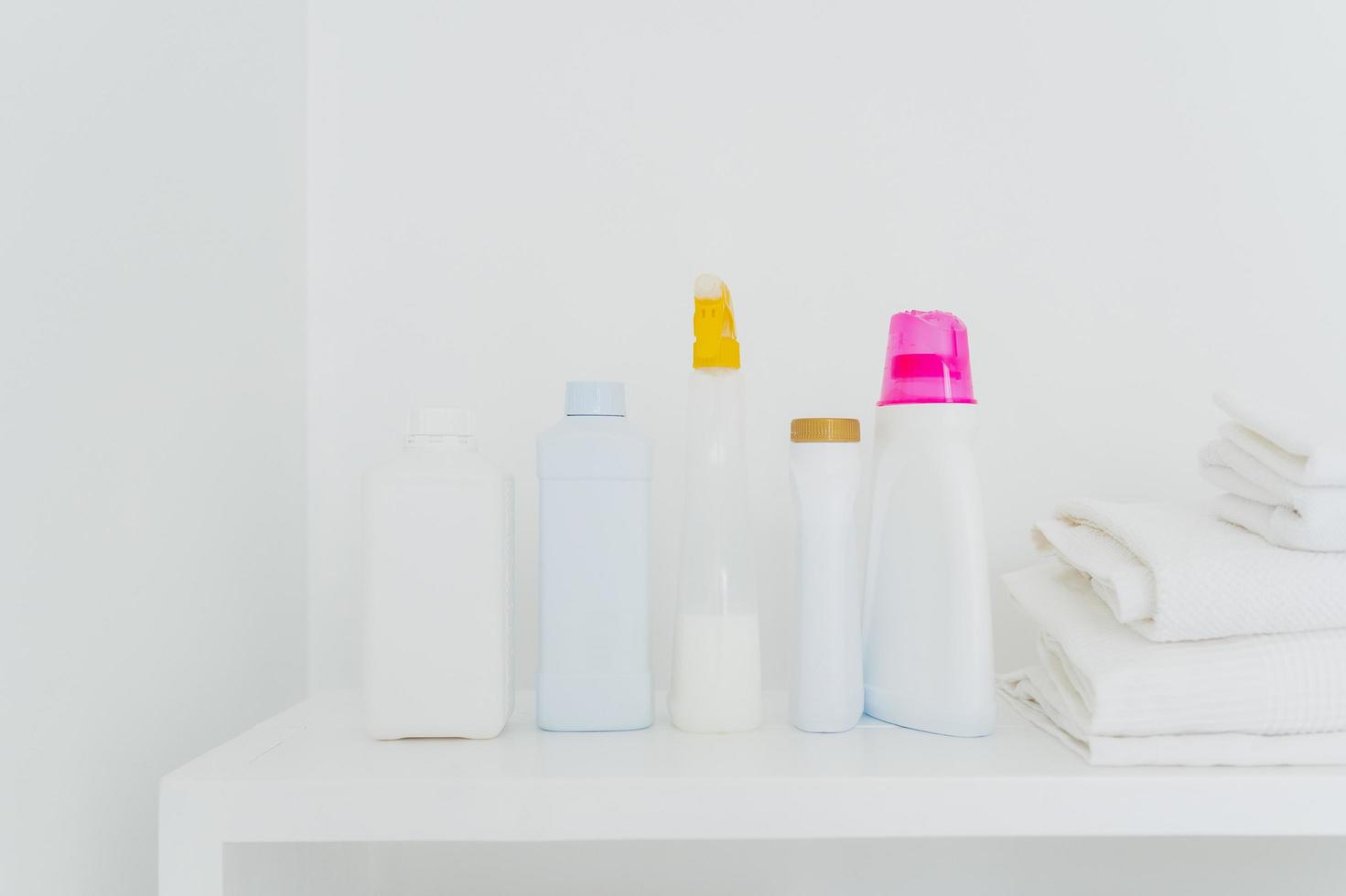 Stack of folded white towels and bottles with detergent against white background. Washing and cleanliness concept. Space for your text photo