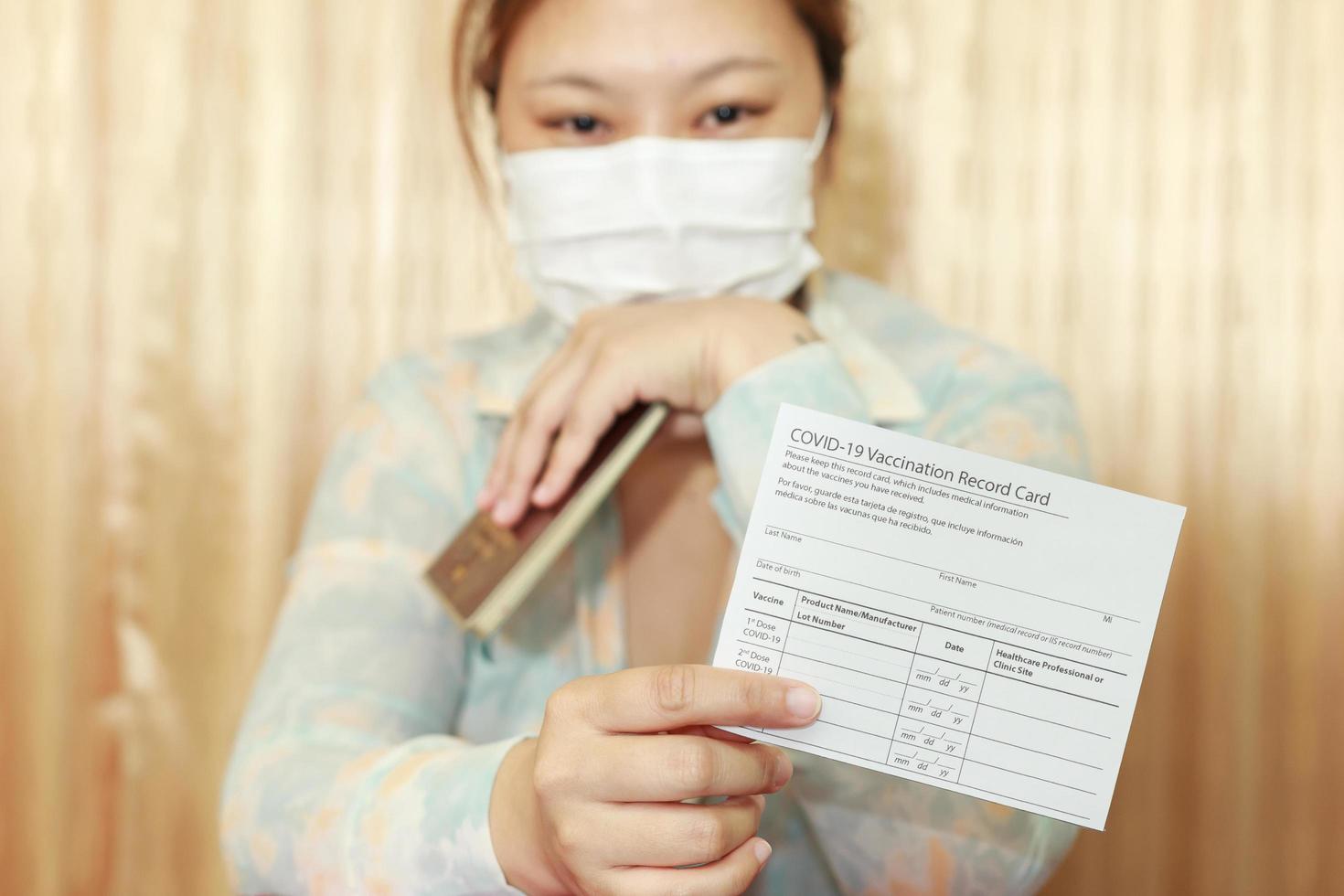 mujer con ropa de viaje con una máscara médica que muestra la tarjeta de registro de vacunación covid-19 y el pasaporte. concepto de viaje con vacunación.enfoque selectivo. foto