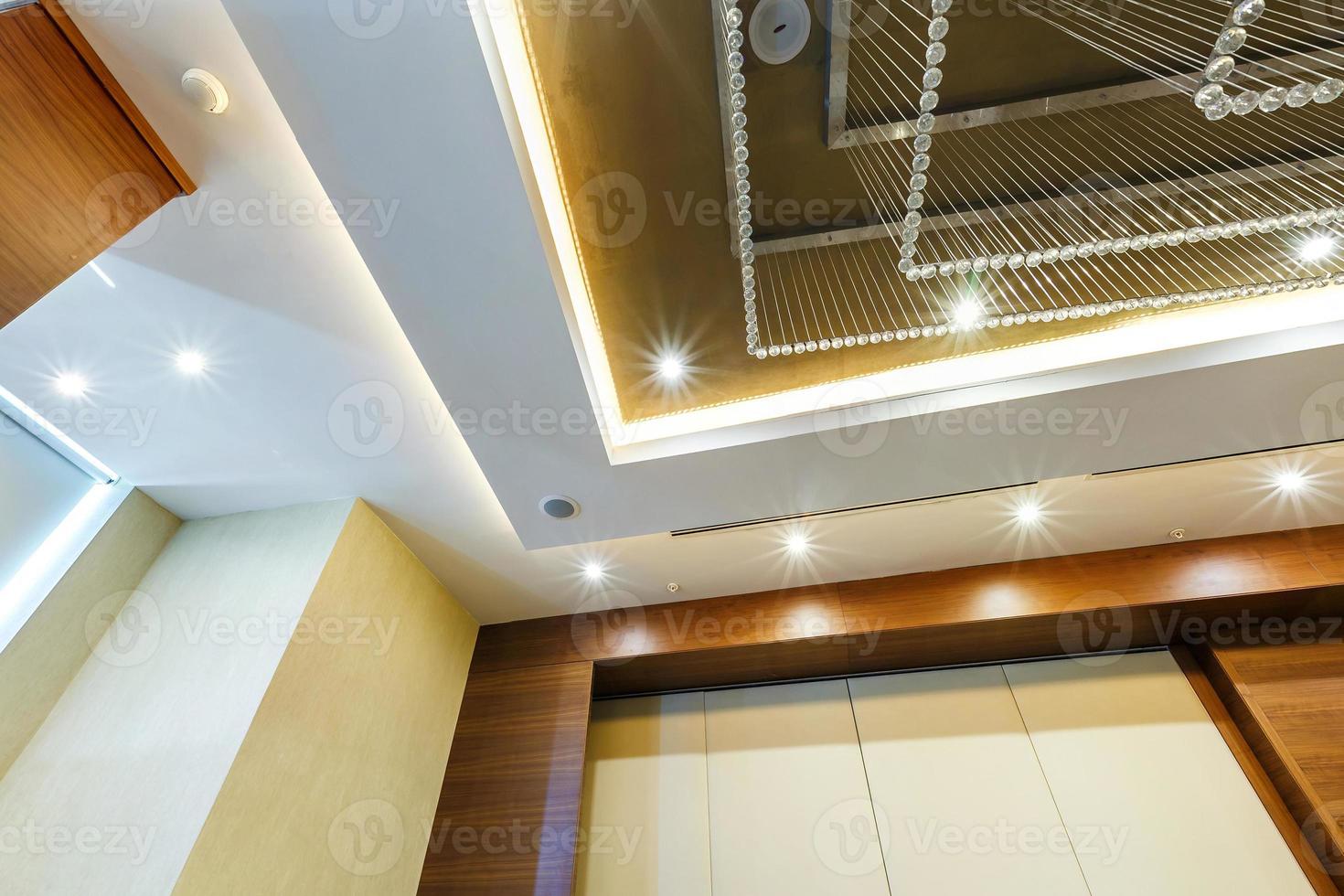 look up on suspended ceiling with halogen spots lamps and drywall construction with fire alarm sensor in empty room in apartment or house. Stretch ceiling white and complex shape. photo