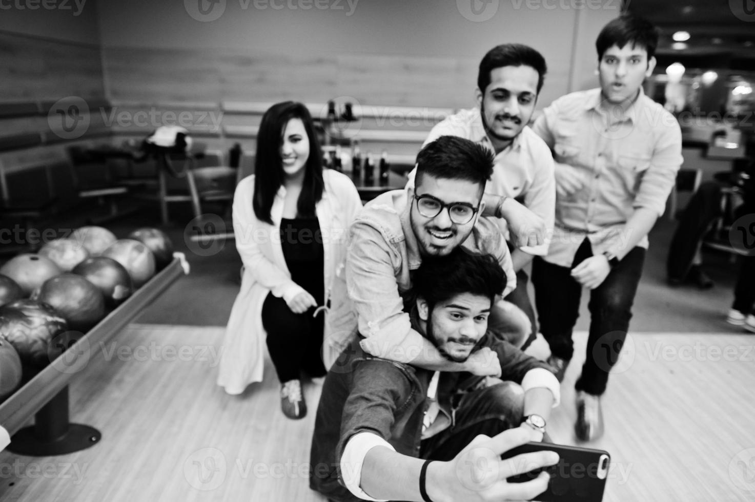 Group of five south asian peoples having rest and fun at bowling club. Making selfie by phone. photo