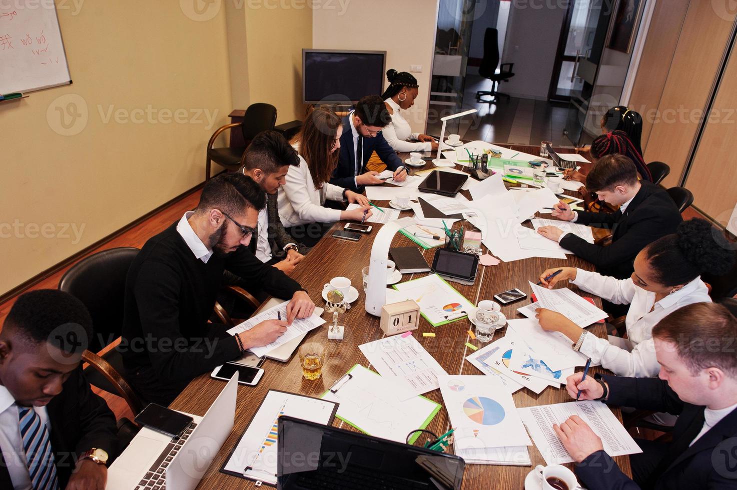 el equipo de negocios multirracial se dirige a la reunión alrededor de la mesa de juntas, trabaja juntos y escribe algo en los papeles. foto