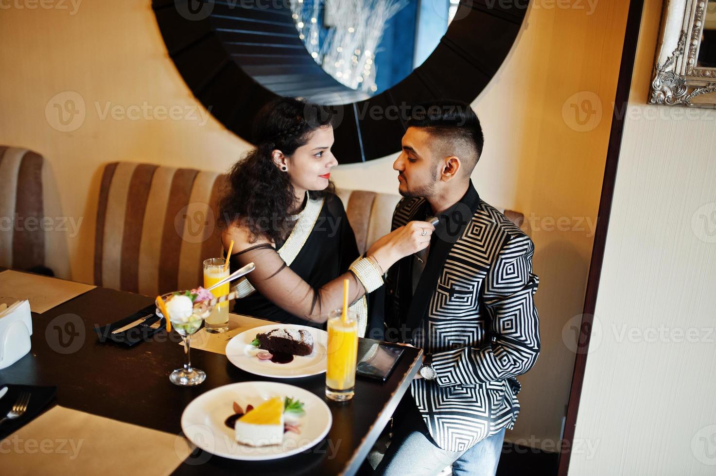 encantadora pareja india enamorada, vestida con sari y traje elegante, posada en el restaurante. la mujer ató la corbata a su hombre. foto
