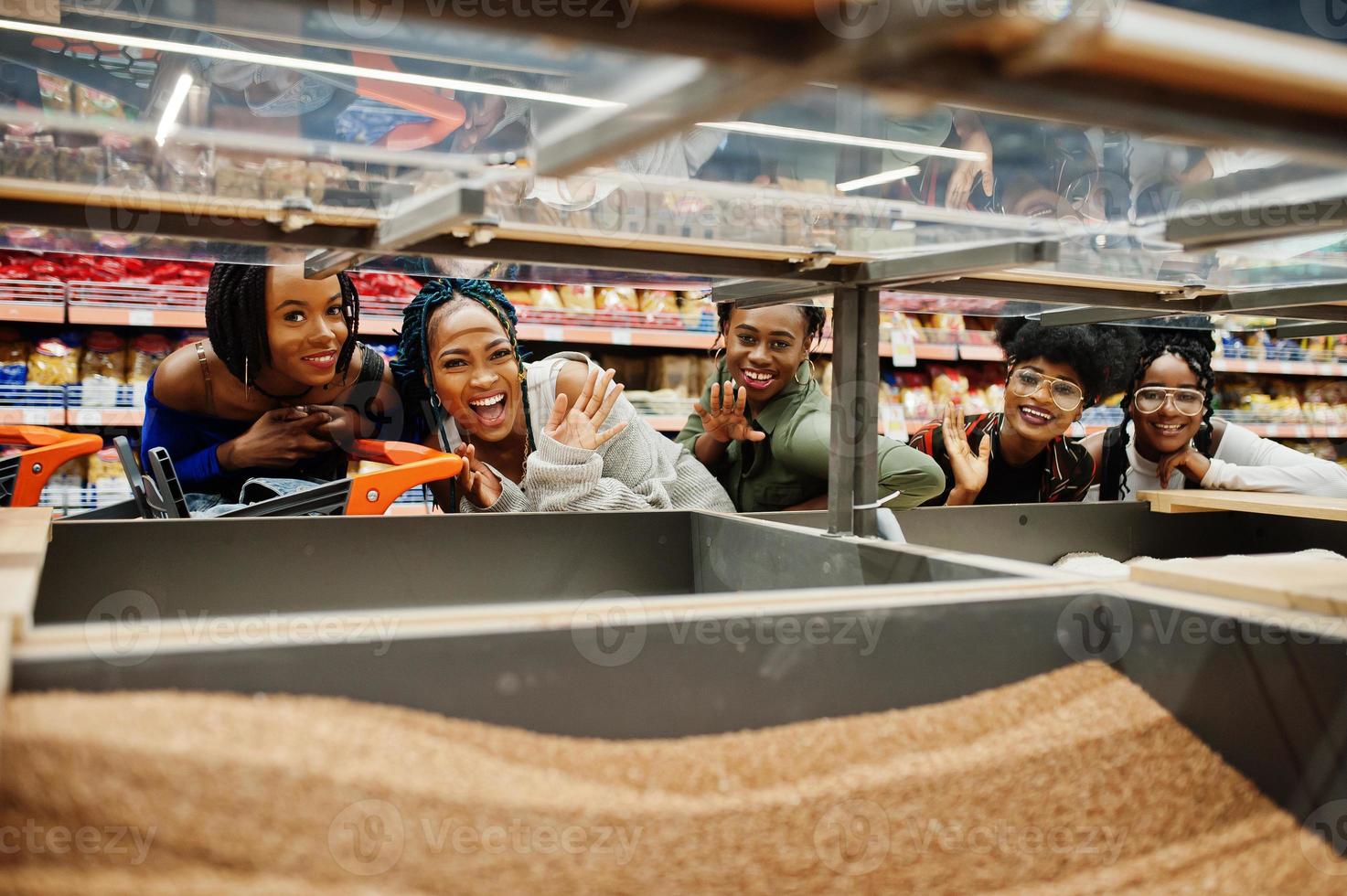 grupo de cinco mujeres africanas divertidas con carritos de compras eligen granos de trigo sarraceno en el supermercado. foto