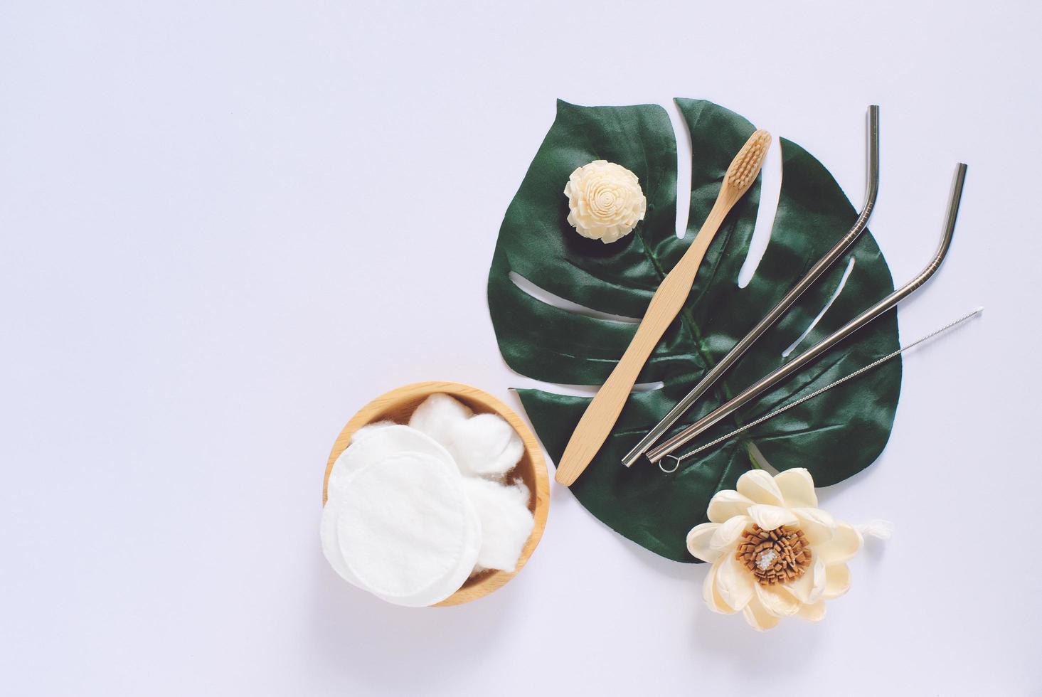 Flat lay of sustainable products, wooden spoon, stainless straw and natural cotton on green plant and white background with copy space, eco friendly and zero waste concept photo