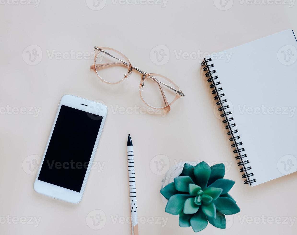 Flat lay of workspace desk with smartphone, notebook, eyeglasses, pen and plant, minimal style photo