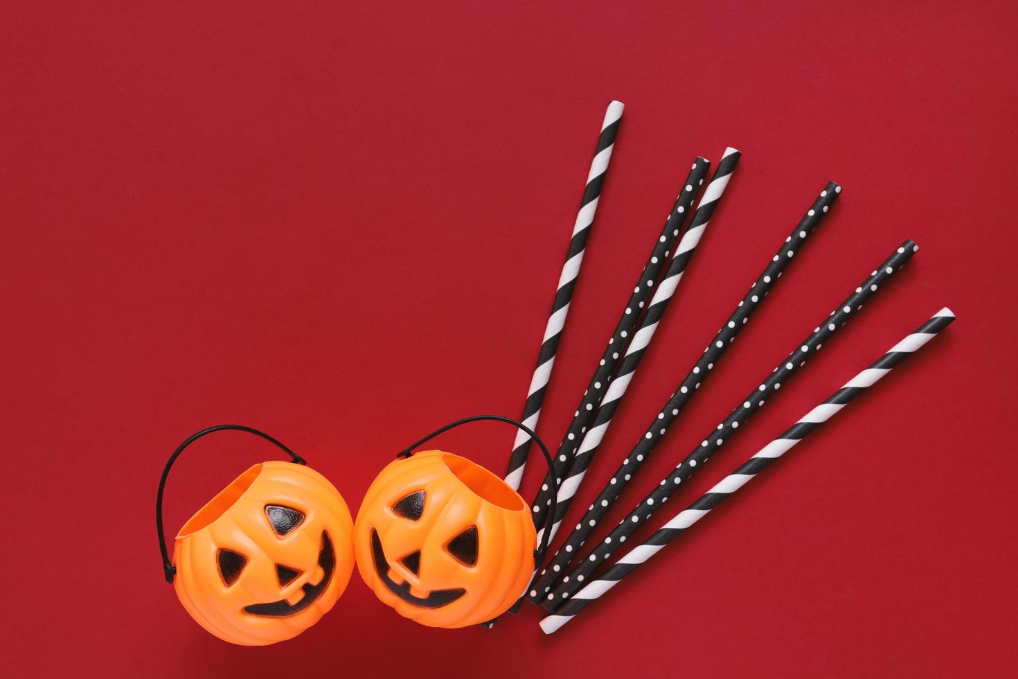 Flat lay style of halloween party concept with decorative pumpkins and black fancy straw on red background, copy space photo