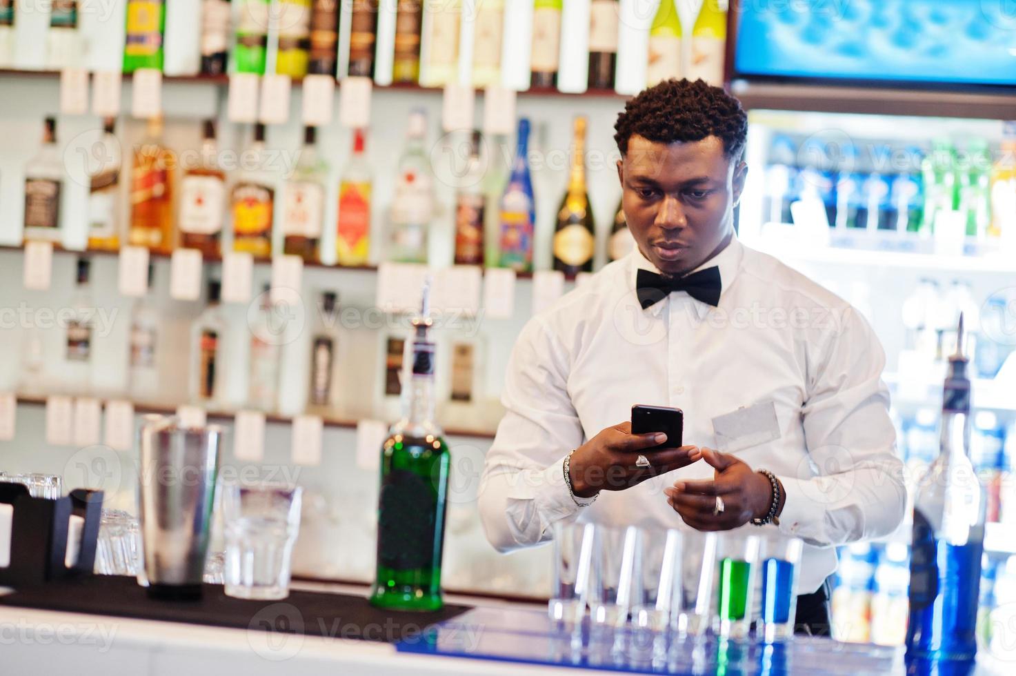 camarero afroamericano en el bar haciendo cócteles en tomas y tomando fotos en el teléfono. preparación de bebidas alcohólicas.