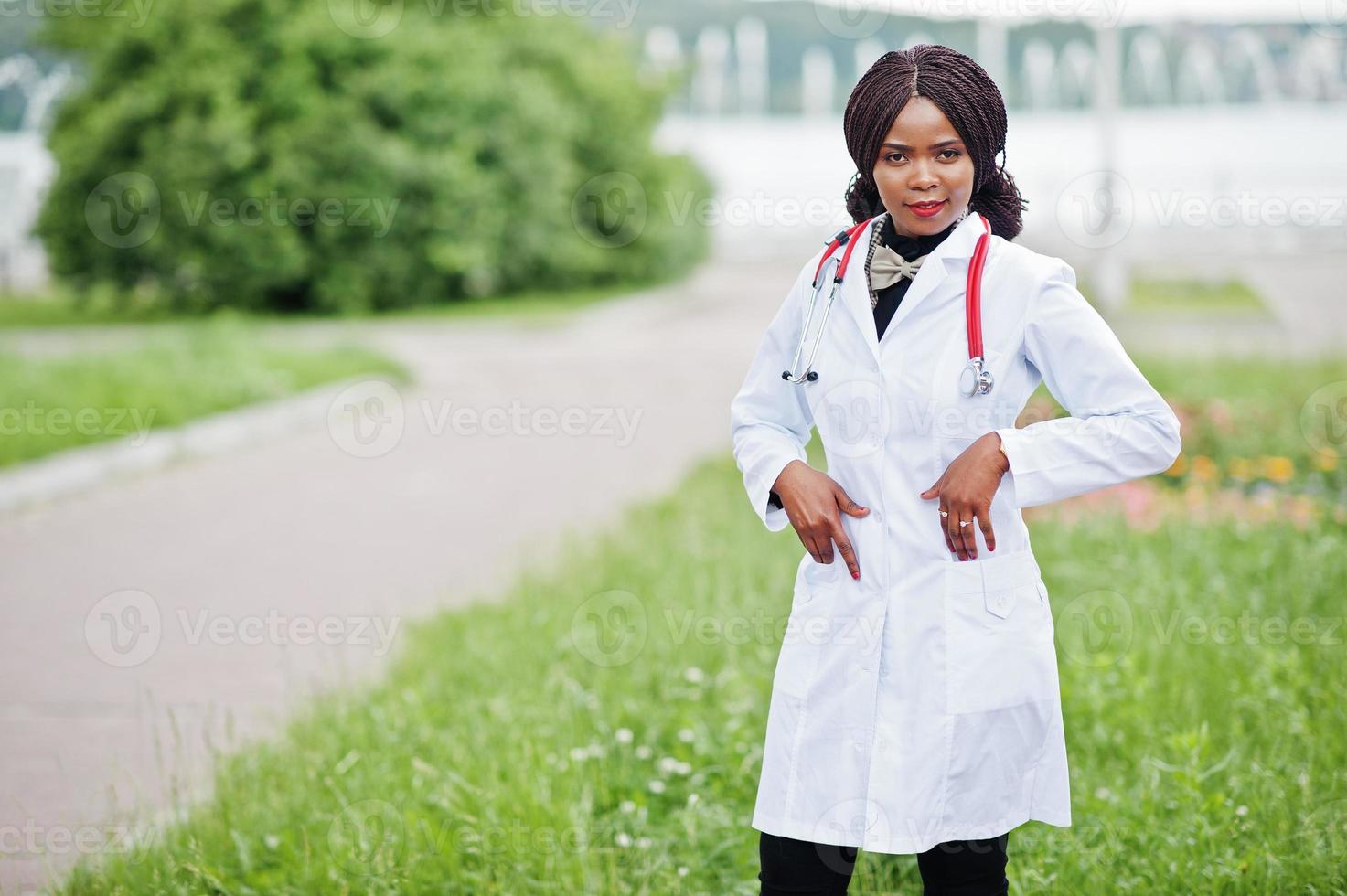Young african american female doctor in white coat with a stethoscope posed outdoor. photo