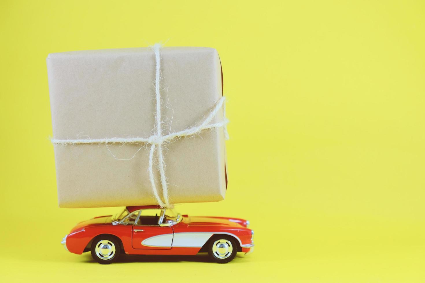 coche de juguete retro rojo que entrega una caja de regalo para la temporada navideña sobre fondo amarillo con espacio para copiar foto