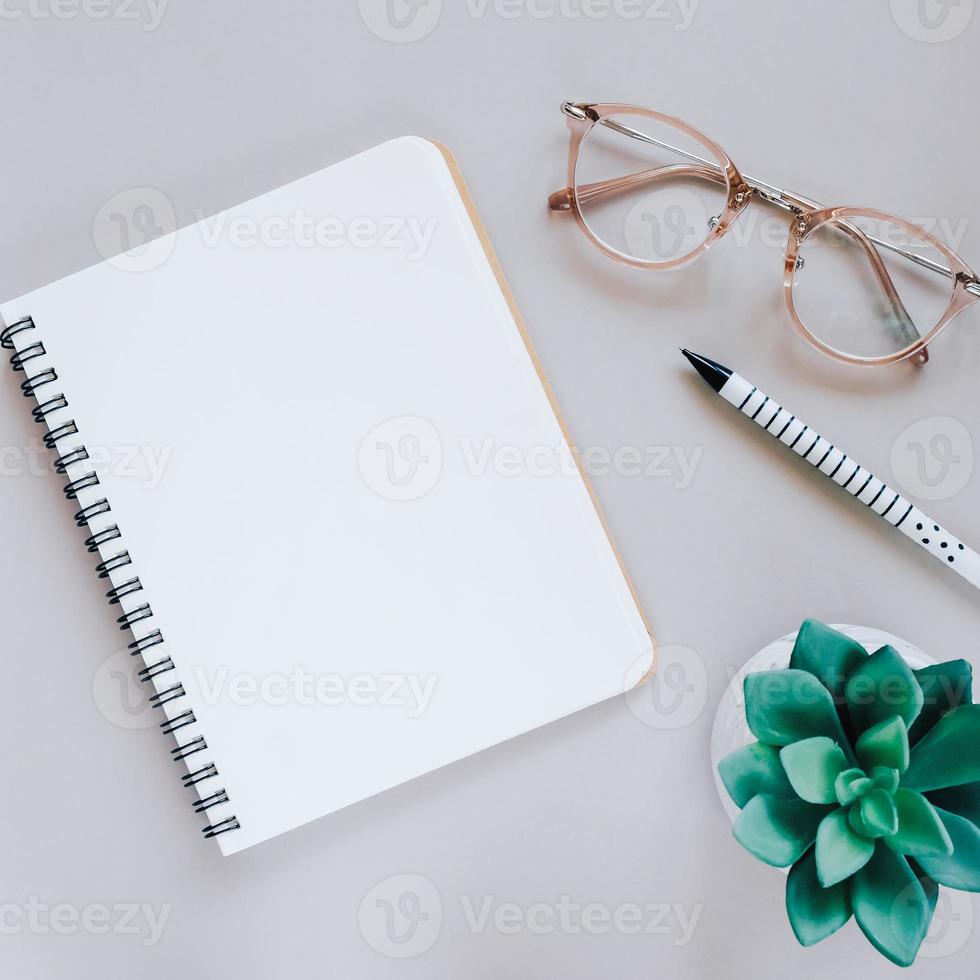 Flat lay of minimal workspace desk with notebook, eyeglasses and green plant, copy space photo