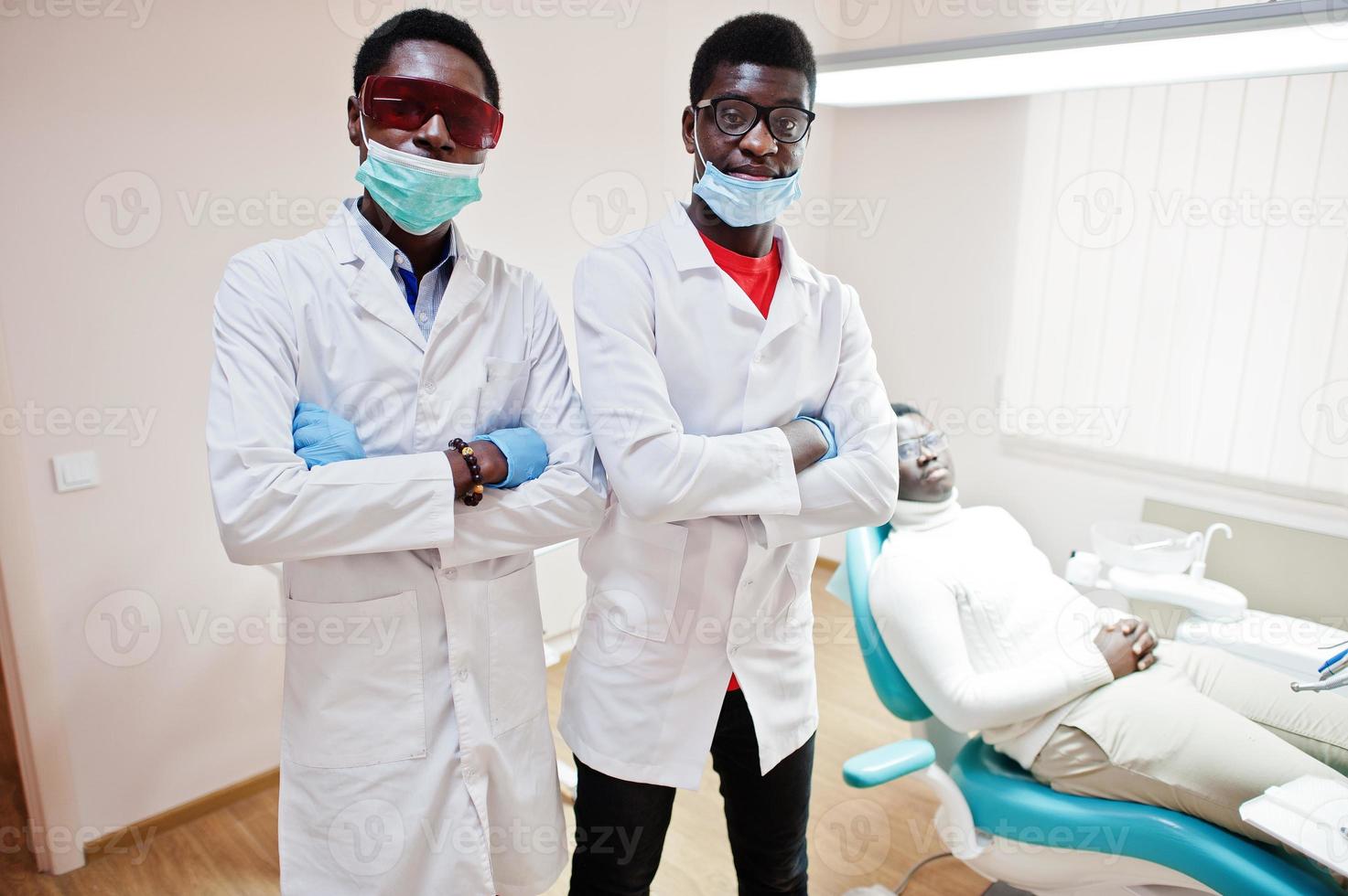 paciente afroamericano en silla dental. oficina de dentista y concepto de práctica médica. dos dentistas profesionales con las manos cruzadas en odontología médica. foto