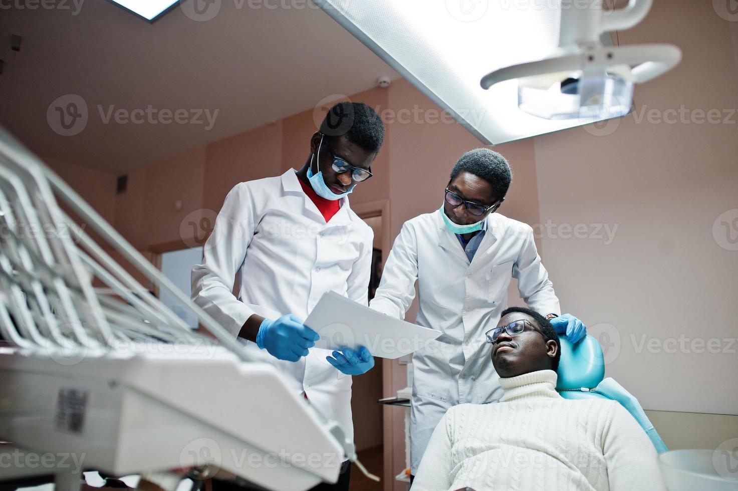 paciente afroamericano en silla dental. oficina de dentista y concepto de práctica médica. dentista profesional ayudando a su paciente en odontología médica. apuntando a la radiografía de los dientes. foto