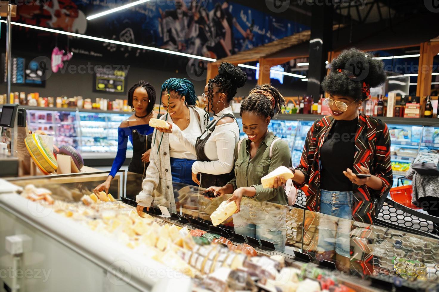 Group of five african womans with shopping carts choose cheese in supermarket. photo