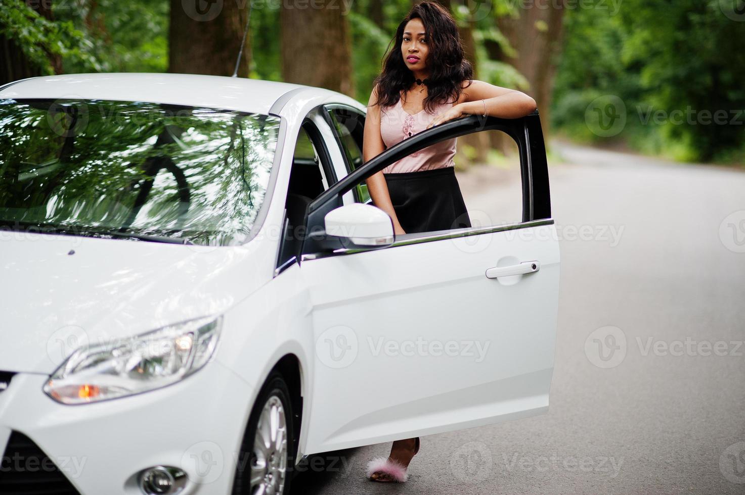 mujer afroamericana posó contra un auto blanco en un camino forestal. foto