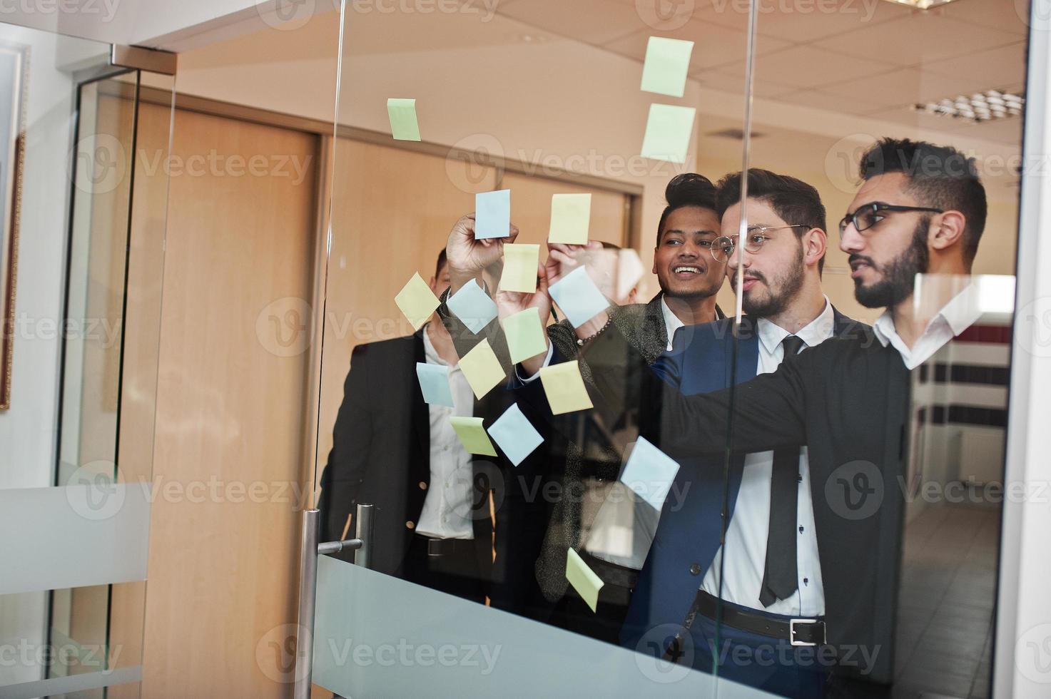 Business mans pointing on glass with colorful paper notes. Diverse group of male employees in formal wear using stickers. photo