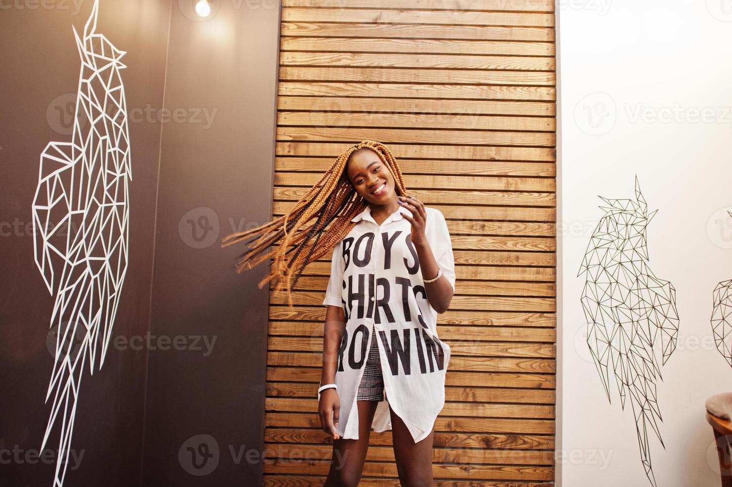 Beautiful african woman in stylish casual clothes posing against angel wings wall. She moving her hair dreadlocks. photo