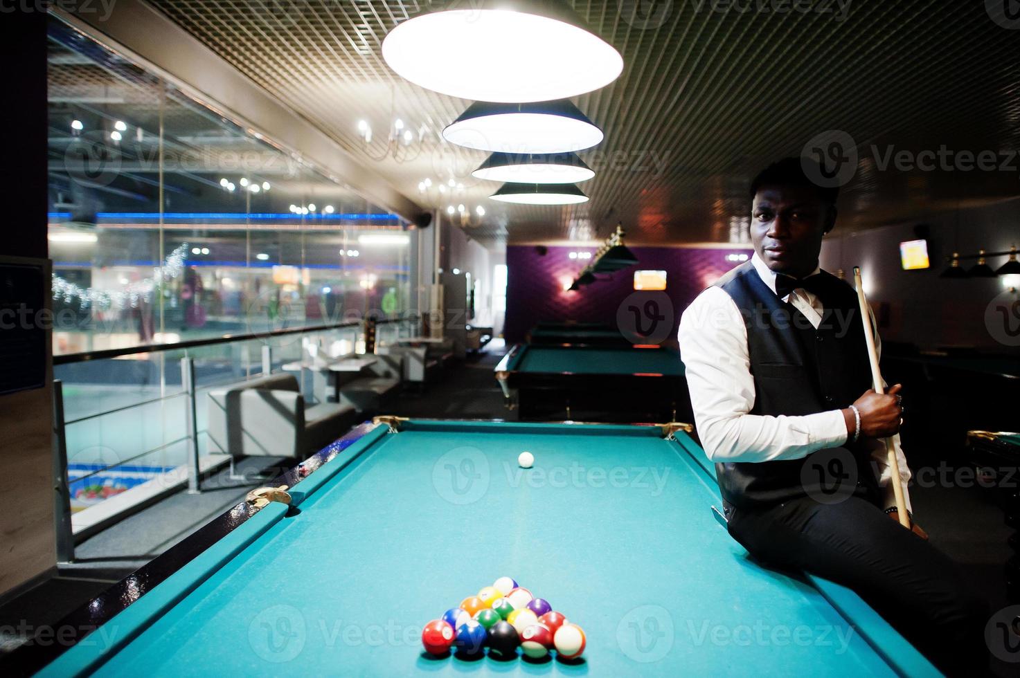 Young handsome african man wearing white shirt, black vest and bow tie play pool billiard. photo