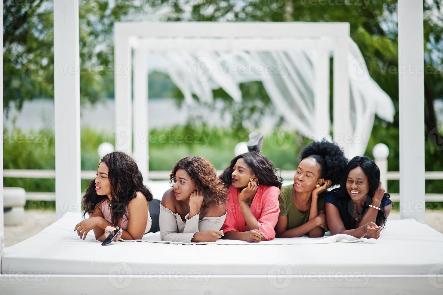 grupo de cinco chicas afroamericanas relajándose en una hermosa cabaña junto a la piscina junto a un complejo de lujo. foto
