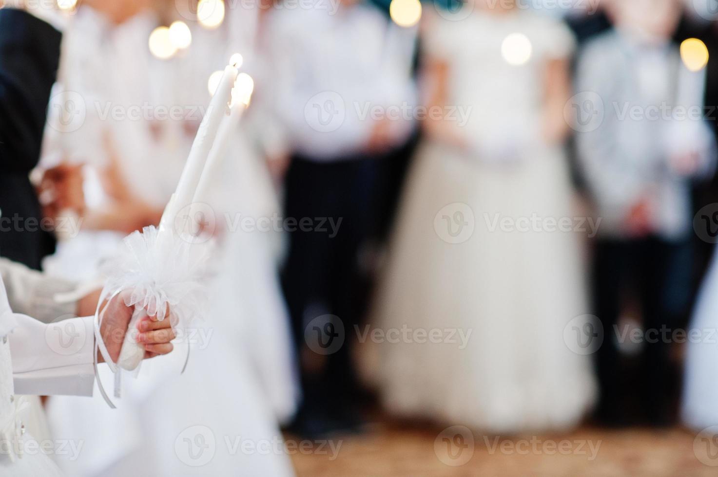 niña de blanco sostenga una vela en la mano en la primera comunión. foto