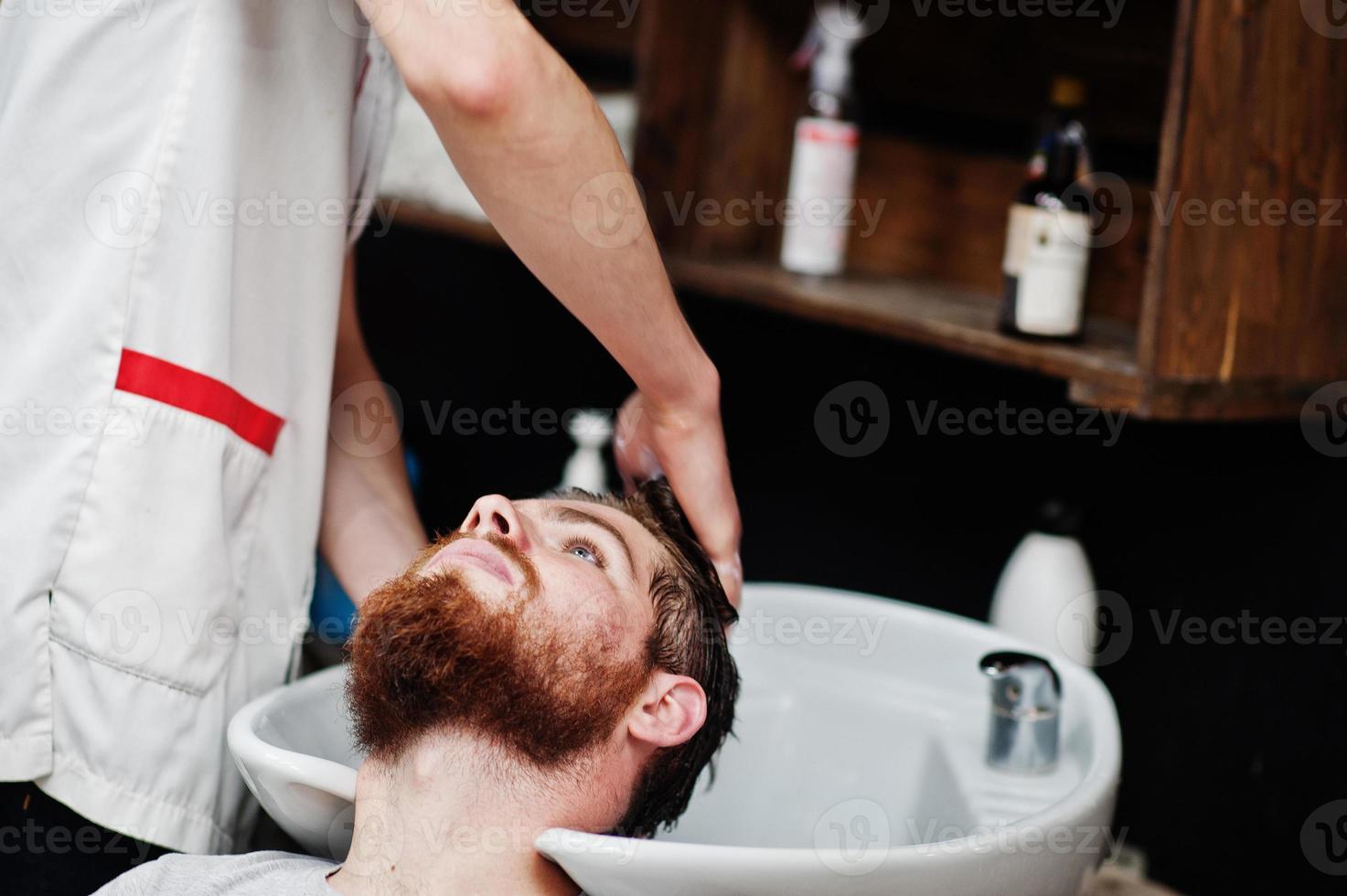 joven barbudo lavando la cabeza por el peluquero mientras se sienta en una silla en la barbería. alma de barbero. foto