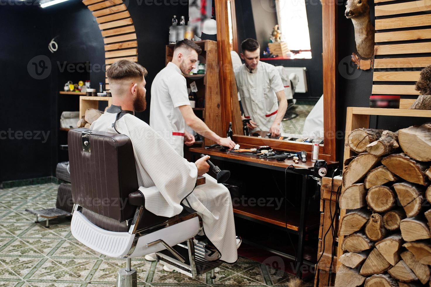 un joven barbudo que se corta el pelo con un peluquero mientras se sienta en una silla en la barbería. alma de barbero. foto