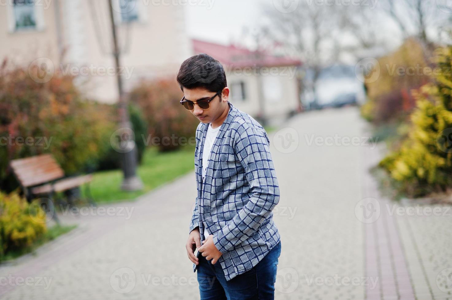 un joven indio elegante con gafas de sol usa una pose informal al aire libre. foto