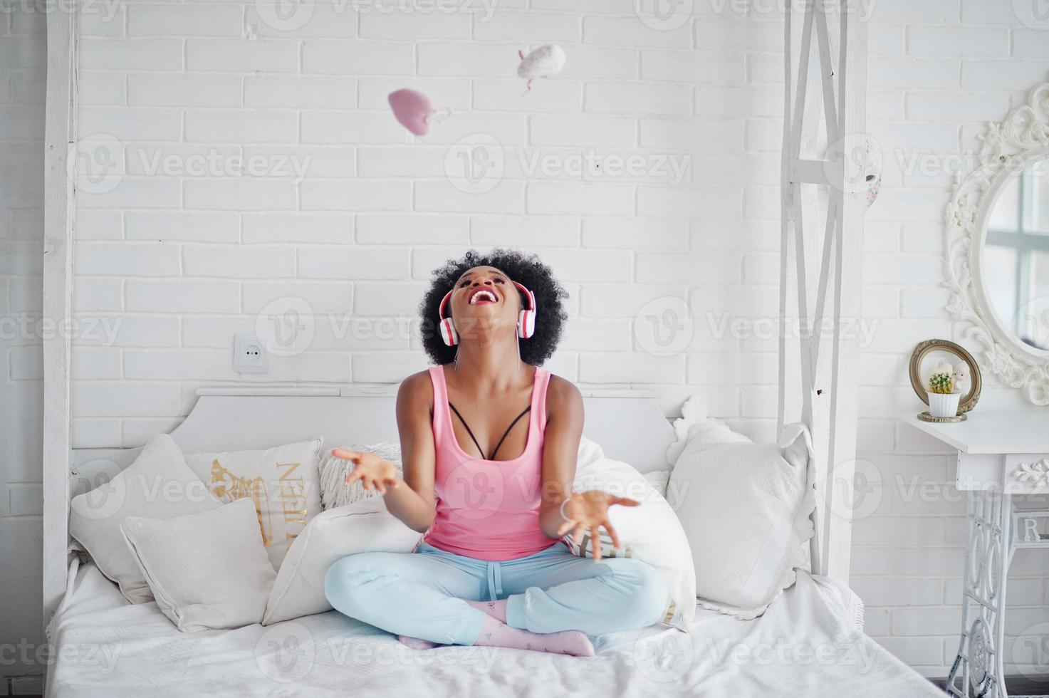 Young african american woman sitting in bed and listen music on earphones. photo