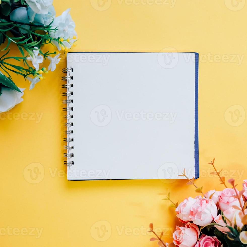 Flat lay of minimal workspace blank notebook with flower on yellow background, spring and summer concept photo