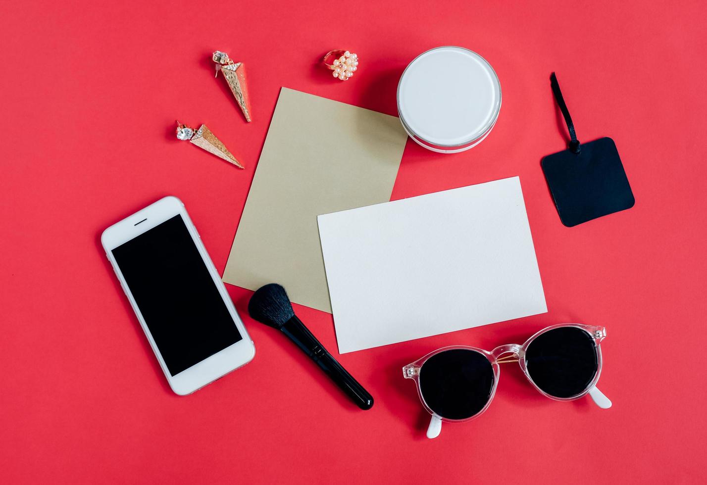 Flat lay of feminine items with cosmetics and accessories with blank card on red background, top view with copy space photo