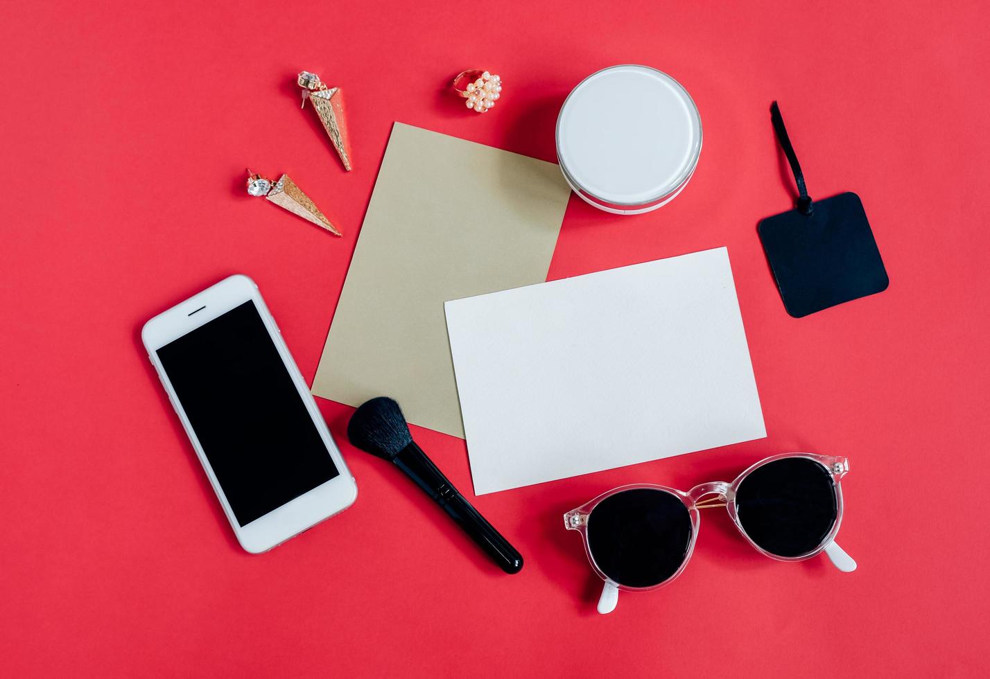 Flat lay of feminine items with cosmetics and accessories with blank card on red background, top view with copy space photo