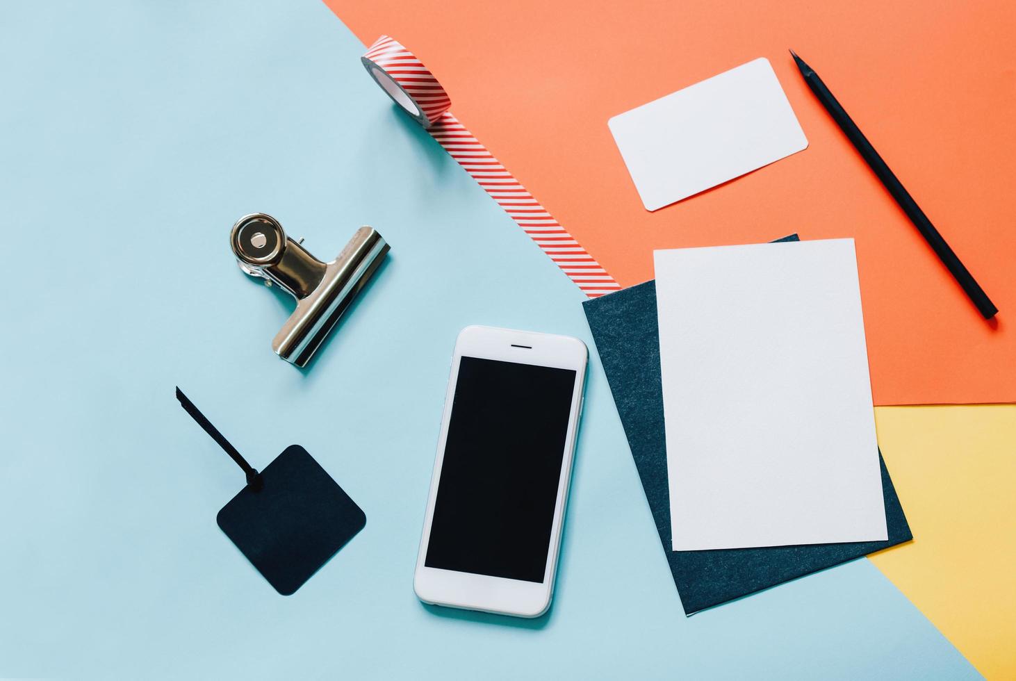 escritorio de espacio de trabajo creativo de estilo plano con teléfono inteligente, sobre en blanco, gafas de sol y cinta adhesiva sobre fondo colorido moderno foto