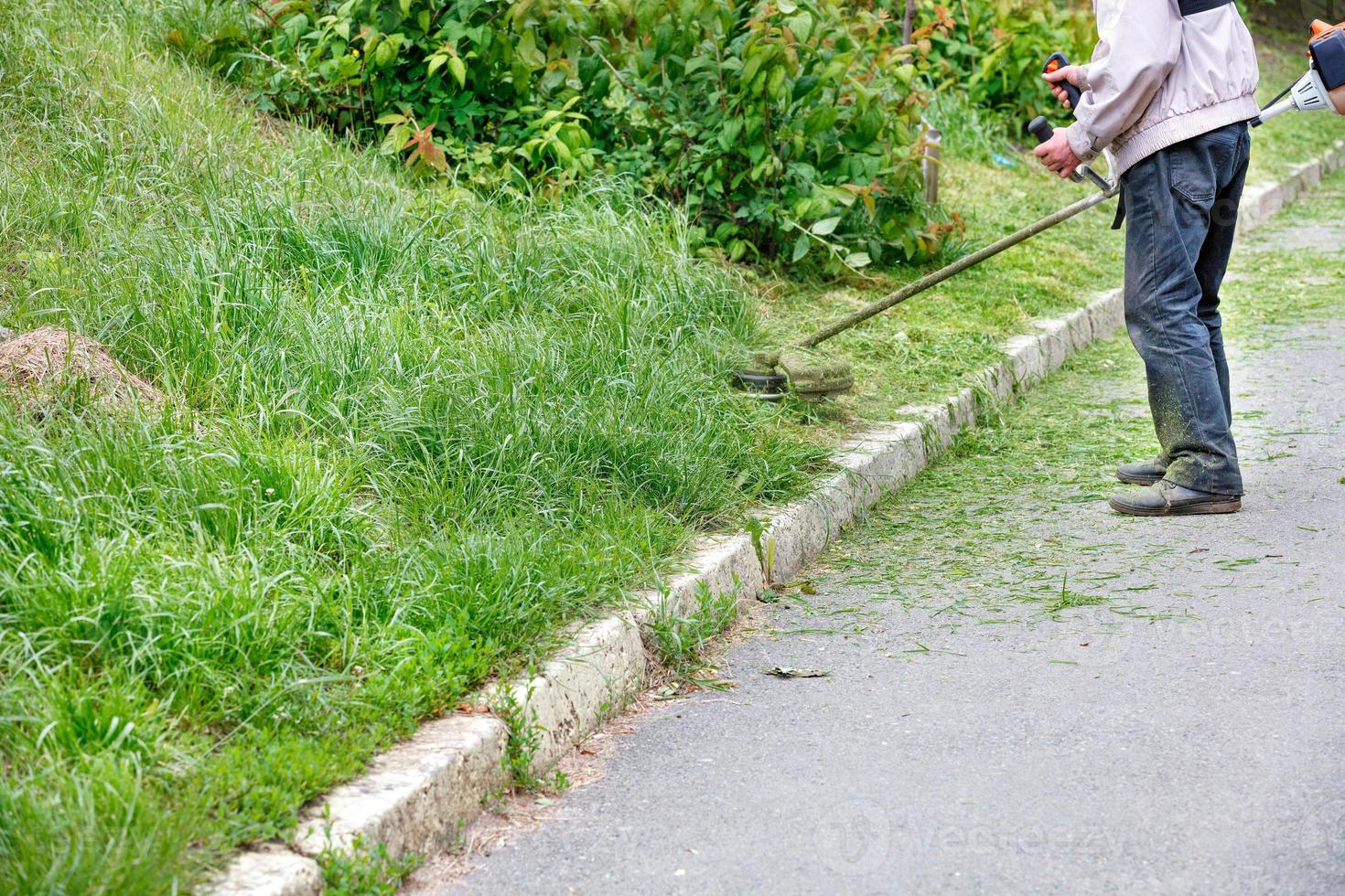 A utility worker mows tall green grass with a petrol trimmer mower. photo