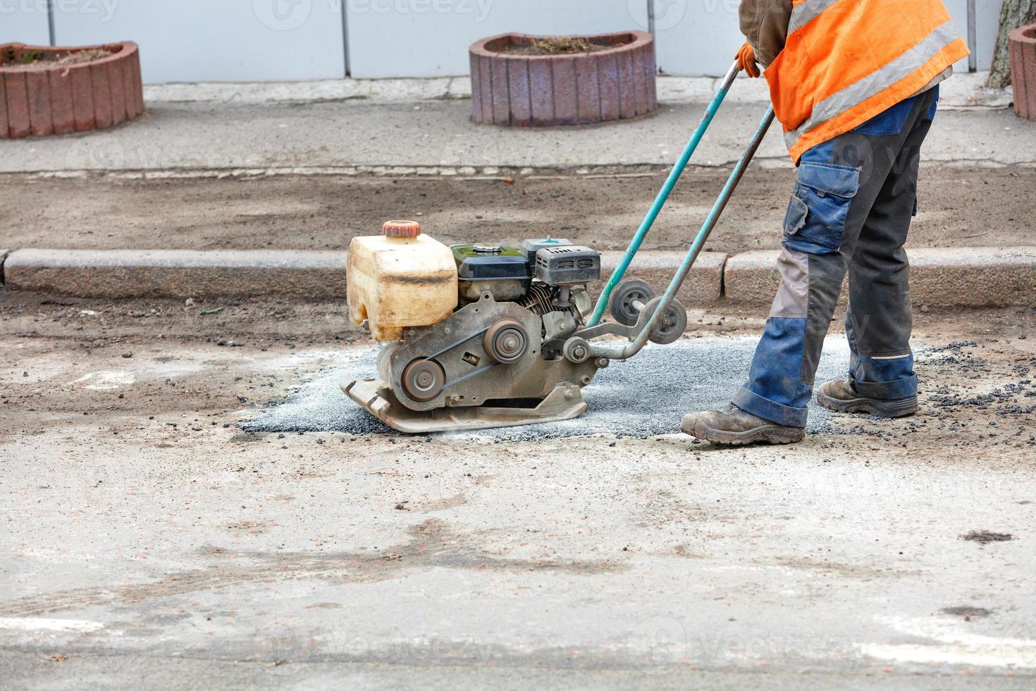 A road worker is patching up a pothole in an old road using an old petrol plate compactor. photo