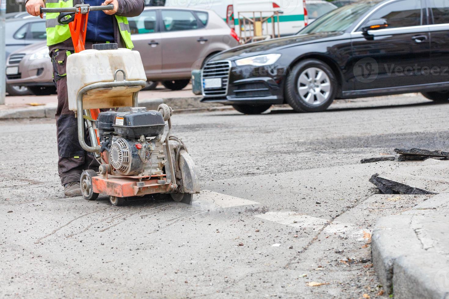 A road worker cuts with a gasoline cutter the destroyed old asphalt on the roadway for the subsequent repair of the road surface. photo