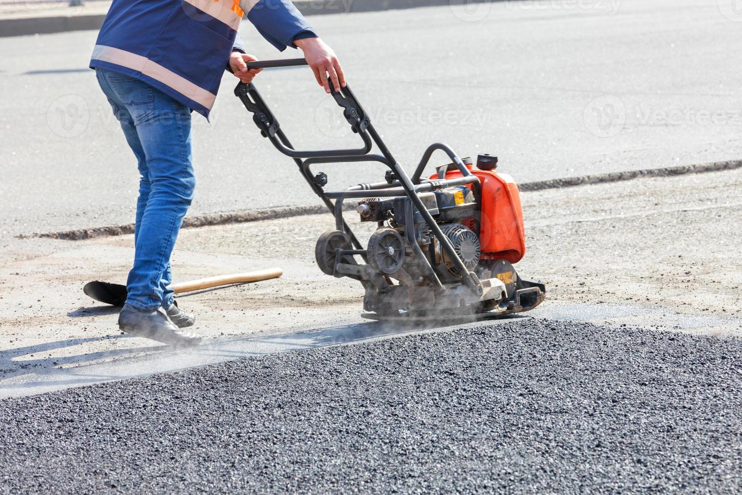 un trabajador de mantenimiento de carreteras compacta asfalto con un compactador vibratorio de gasolina. foto