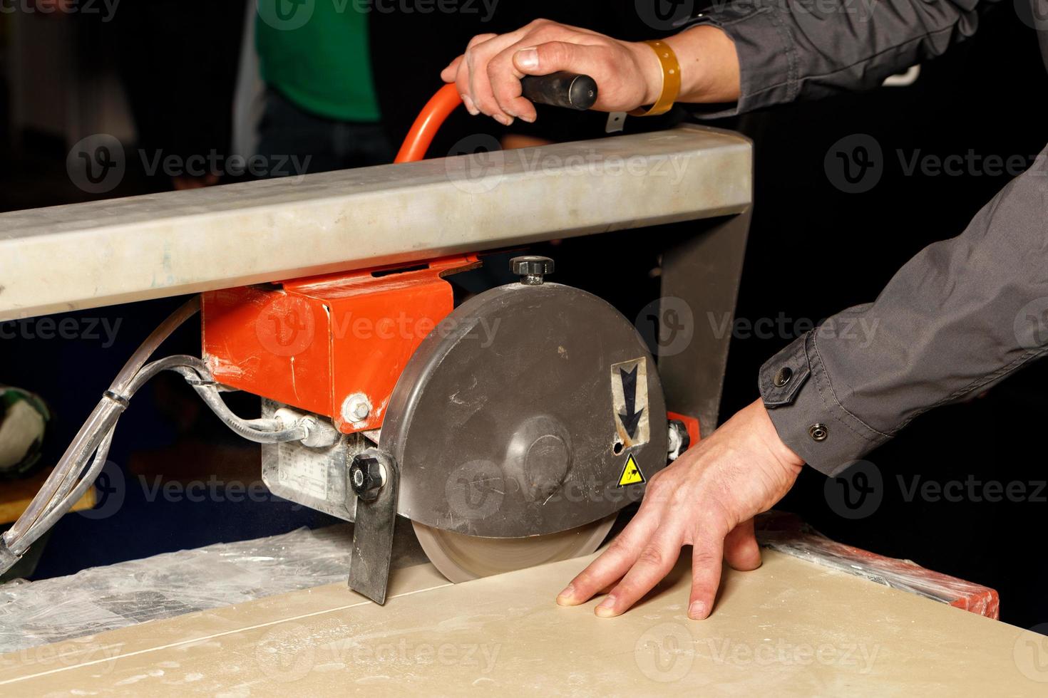 A worker cuts porcelain tiles on an industrial tile cutter with a diamond blade. photo