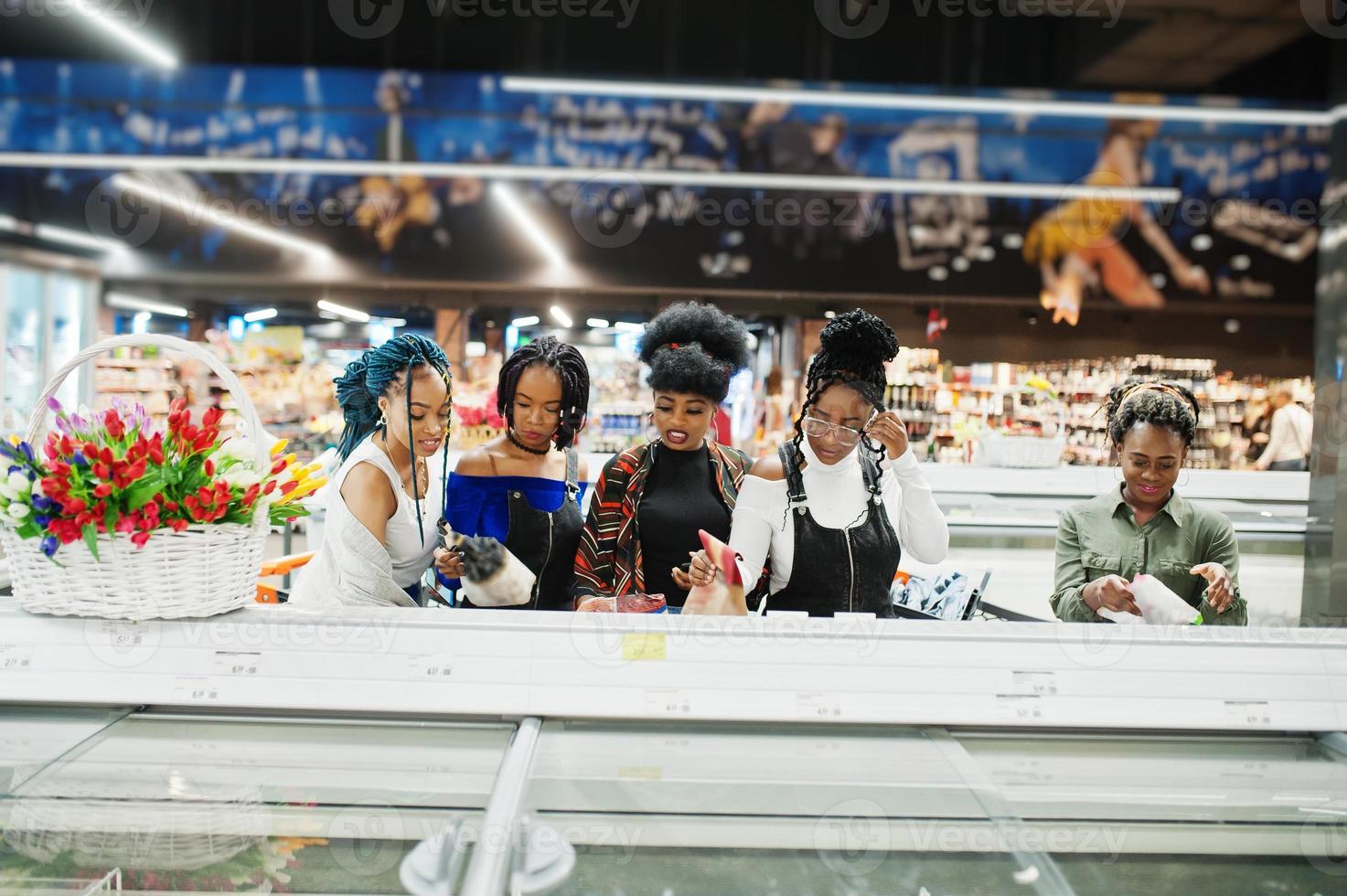 Group of african womans with shopping carts near refrigerator choose packs of dumplings in the supermarket. photo