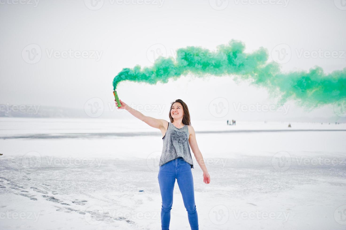 Young girl with green colored smoke bomb in hand in winter day. photo