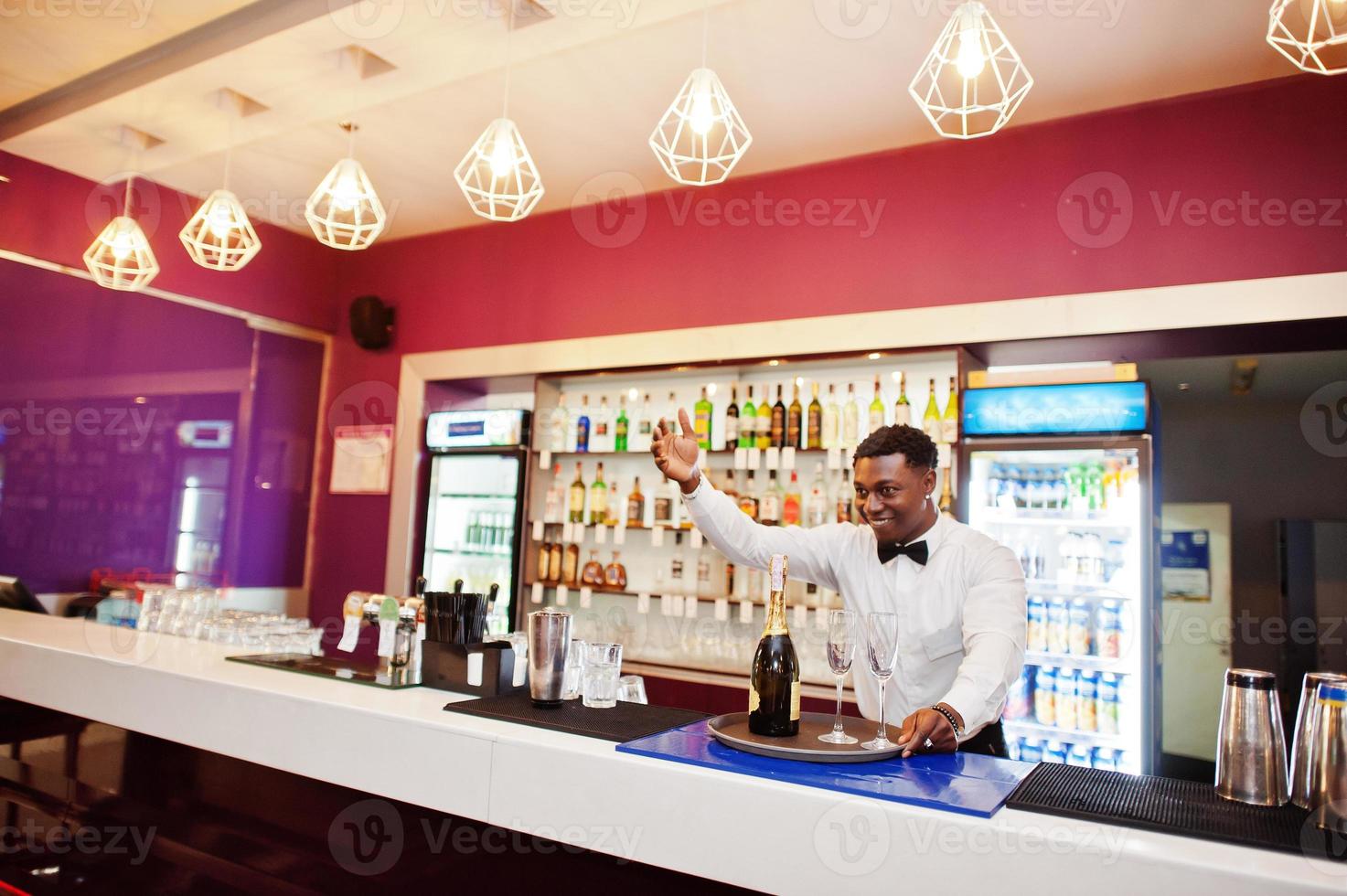 camarero afroamericano en el bar con champán con copas en la bandeja. foto