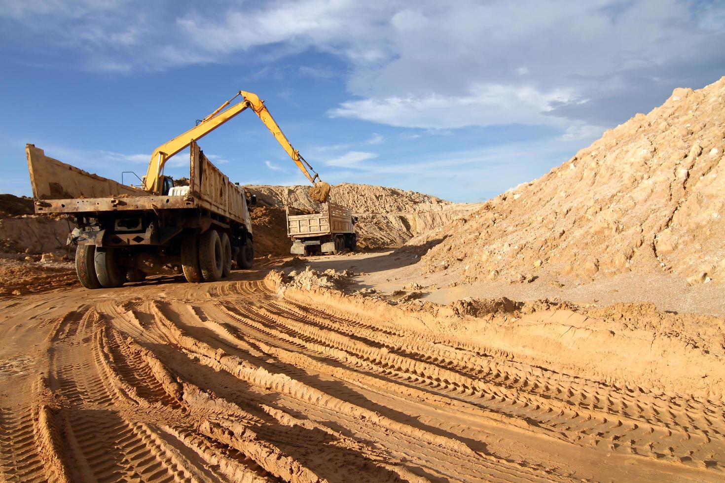 excavadora pesada cargando camión volquete con arena en cantera sobre cielo azul foto