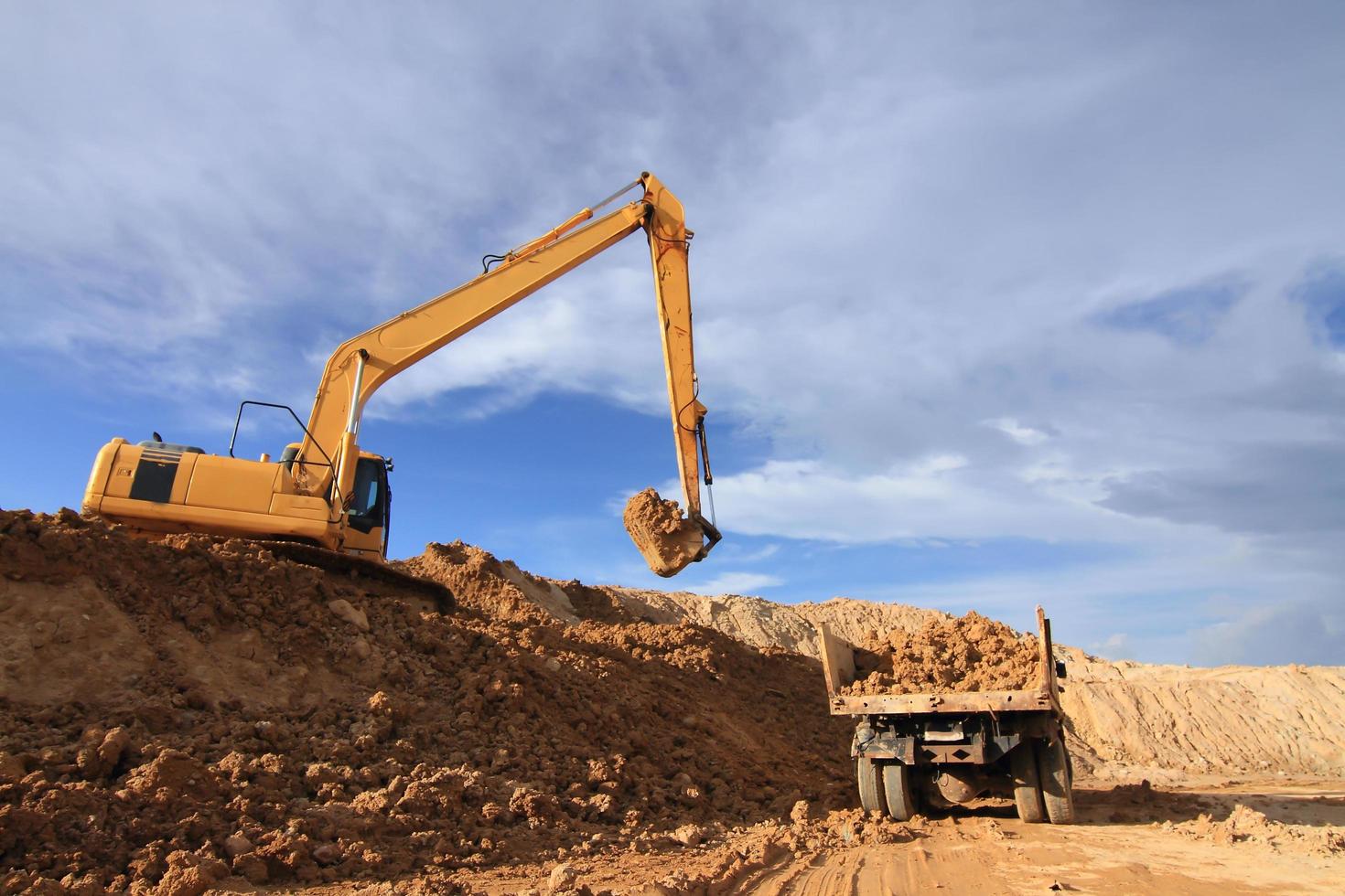 Heavy excavator loading dumper truck with sand in quarry over blue sky photo