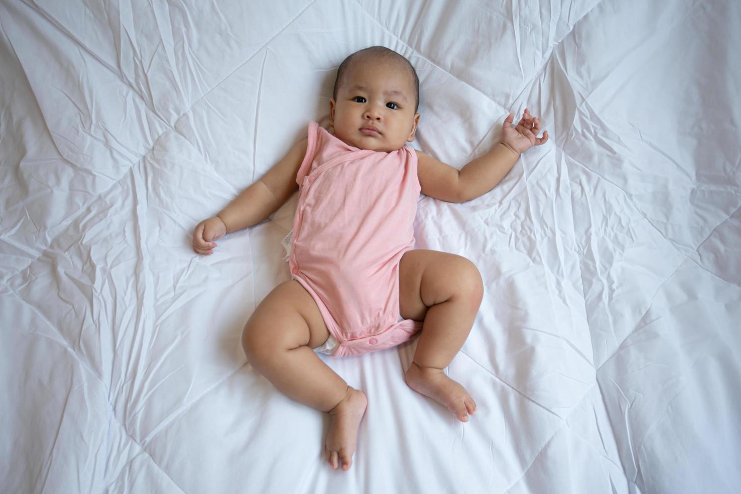 lindo bebé asiático en dormitorio blanco soleado. niño recién nacido descansando en la cama foto