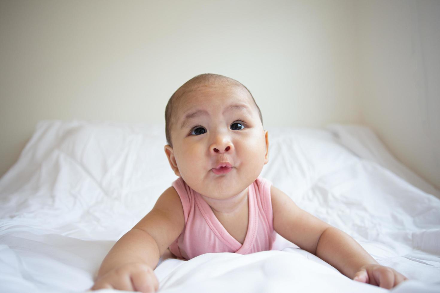 Asian cute baby in white sunny bedroom. Newborn child relaxing on bed photo