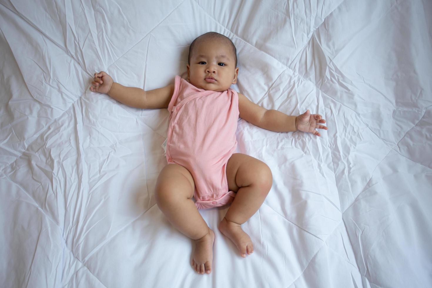 lindo bebé asiático en dormitorio blanco soleado. niño recién nacido descansando en la cama foto