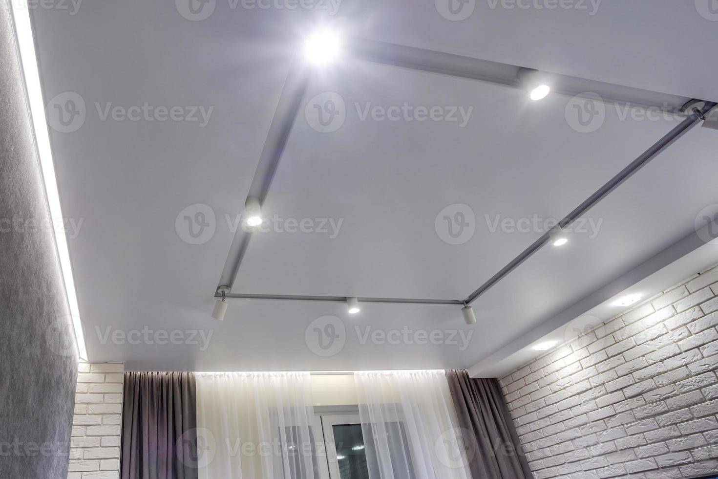 halogen spots lamps on suspended ceiling and drywall construction in in empty room in apartment or house. Stretch ceiling white and complex shape. photo