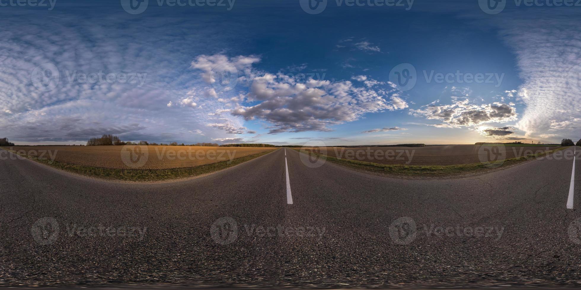 Full spherical seamless panorama 360 degrees angle view on no traffic asphalt road among fields in evening  before sunset with cloudy sky. 360 panorama in equirectangular projection, VR AR content photo