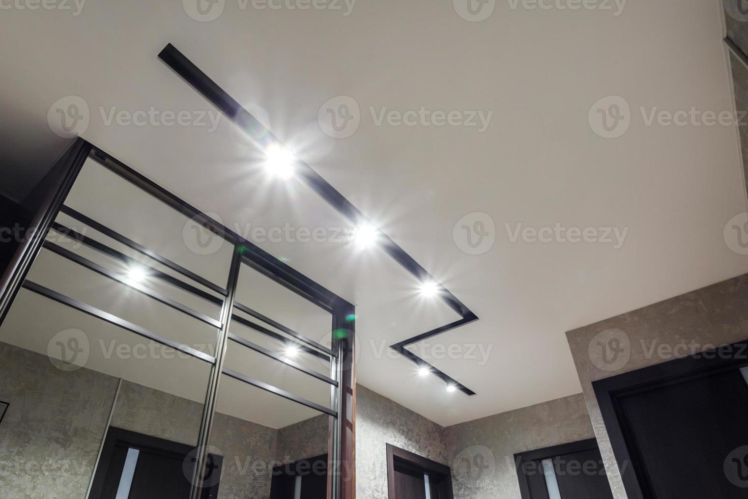 halogen spots lamps on suspended ceiling and drywall construction in in empty room in apartment or house. Stretch ceiling white and complex shape. photo