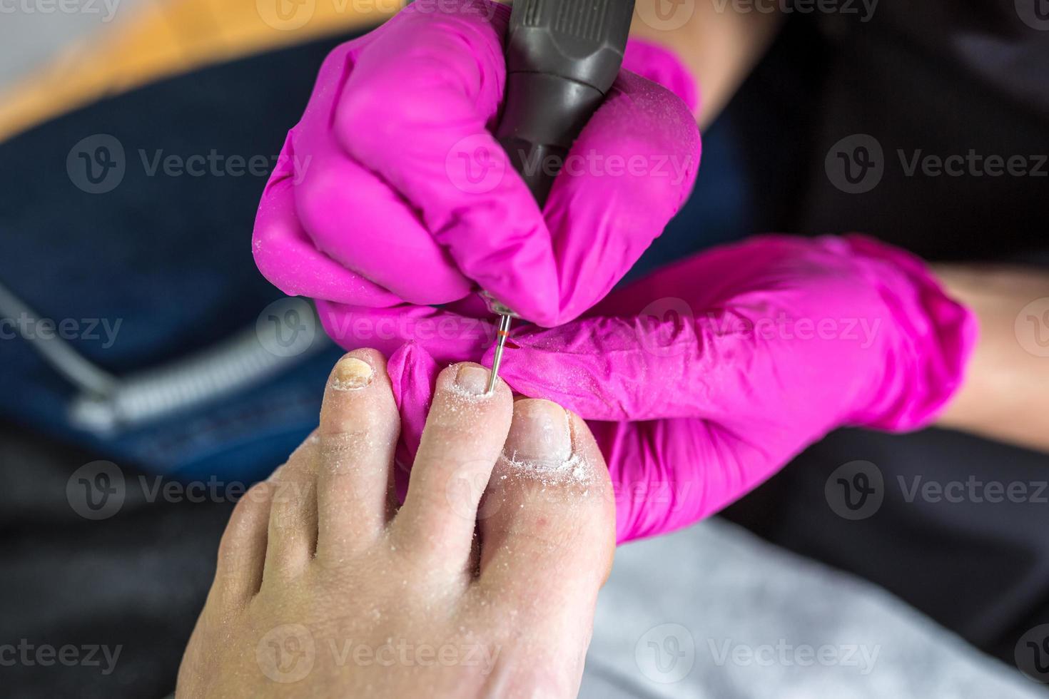 Pedicurist master in pink gloves cuts the cuticle and shellac toe nails in the pedicure salon using drill.  Professional pedicure in cosmetology clinic. Hygiene for feet in beauty salon. photo