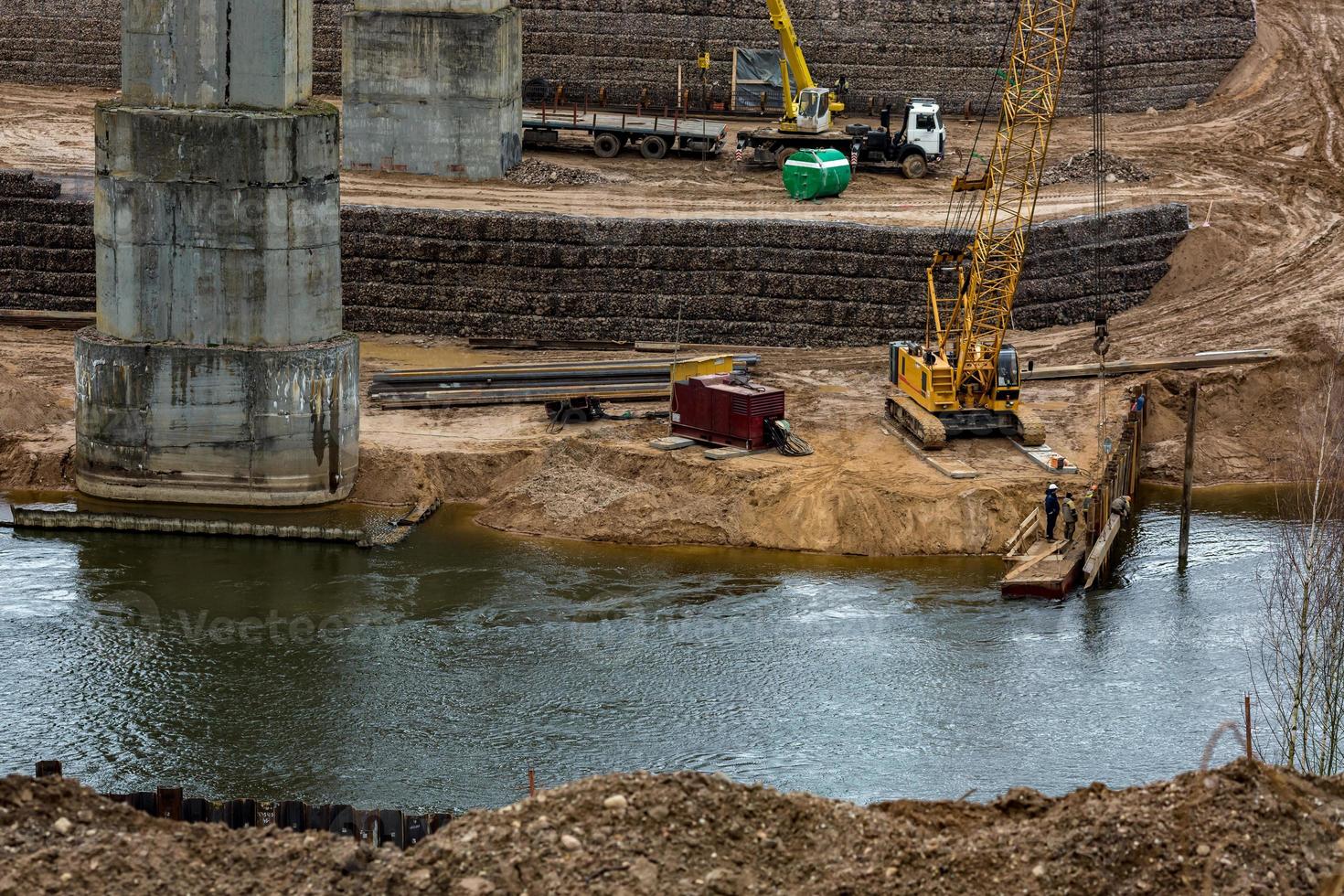 construction or reconstruction of highway concrete bridge over a wide river. construction machinery, trucks and cranes work photo