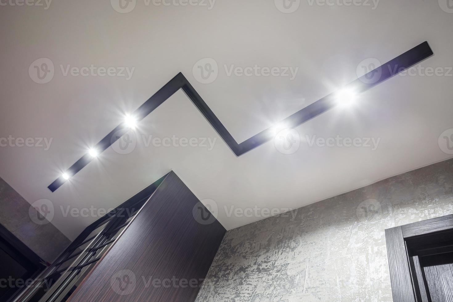 halogen spots lamps on suspended ceiling and drywall construction in in empty room in apartment or house. Stretch ceiling white and complex shape. photo